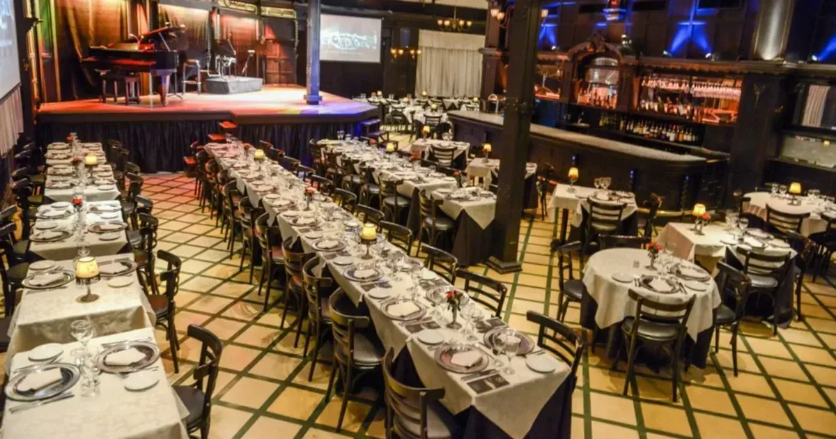 A Buenos Aires tango dinner hall laid with white linen before service, with the stage and piano beyond the tables