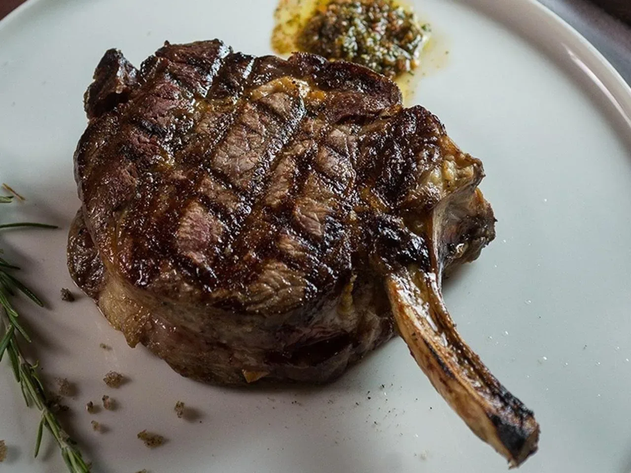 A grilled Argentine steak on the bone, plated with herbs, served as a tango dinner main course