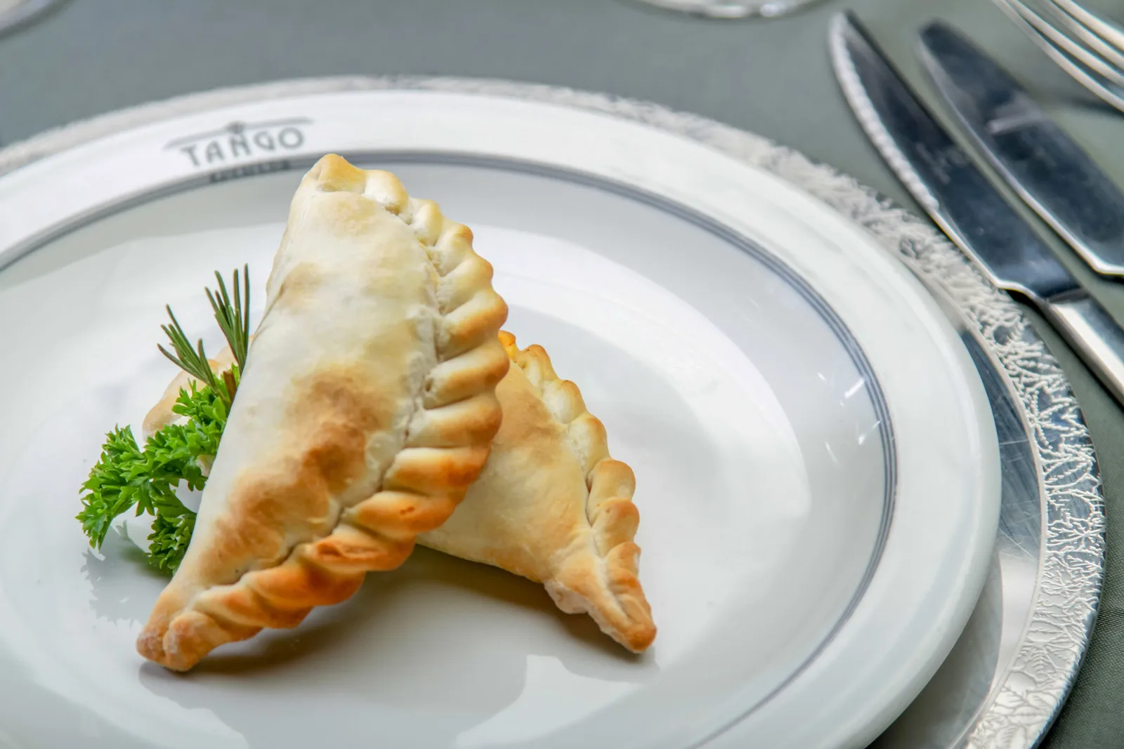 Two baked empanadas and a sprig of parsley on a plate marked Tango