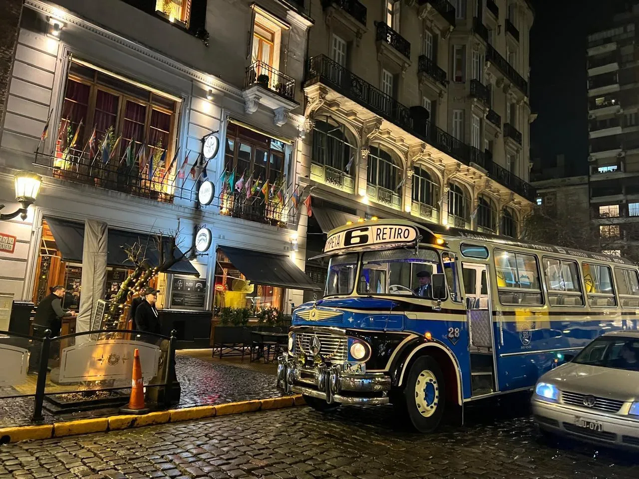 A vintage blue and cream bus parked on a cobbled Buenos Aires street outside a tango venue at night