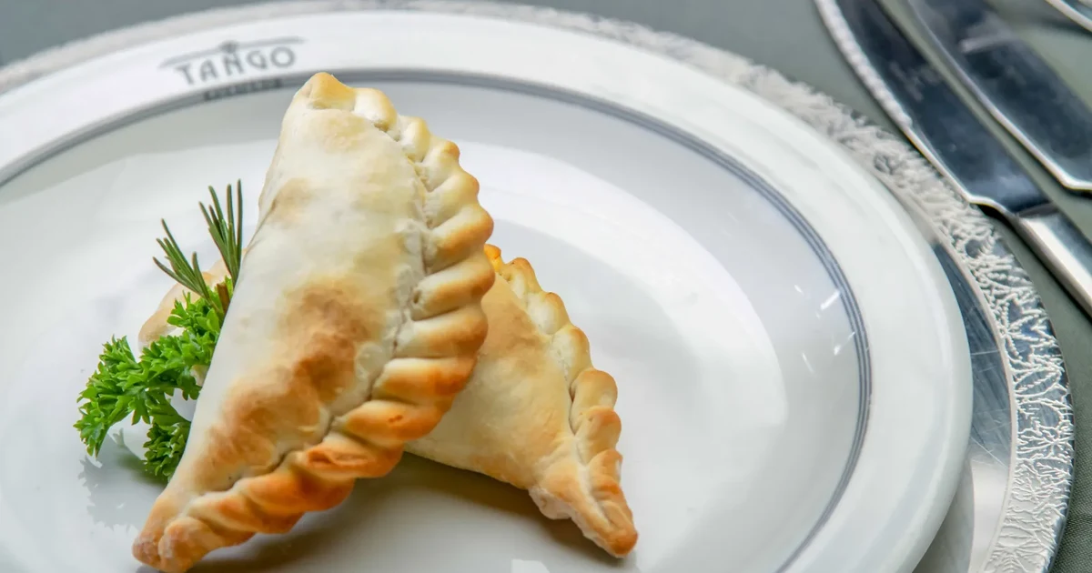 Two baked Argentine empanadas on a plate marked Tango, served as a tango dinner show starter